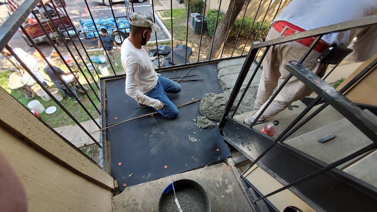 Workers laying concrete on small balcony.