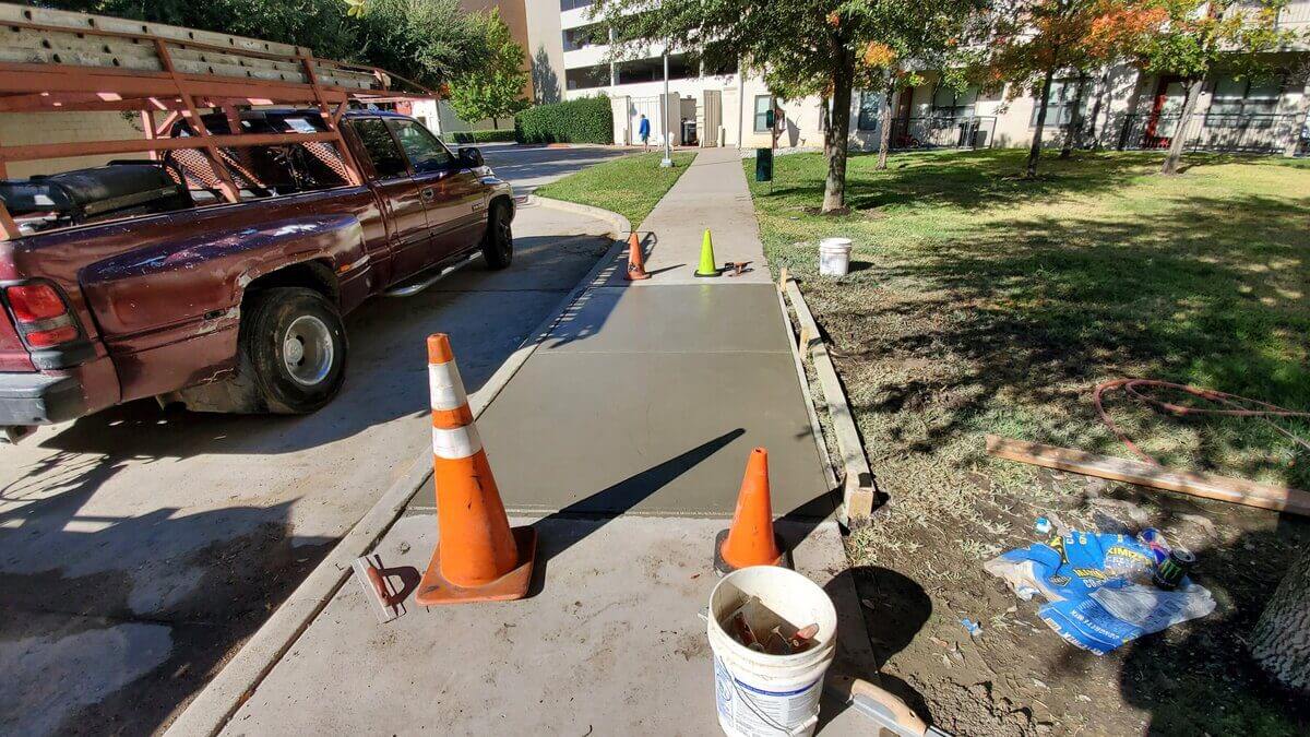 Wet concrete sidewalk with traffic cones.