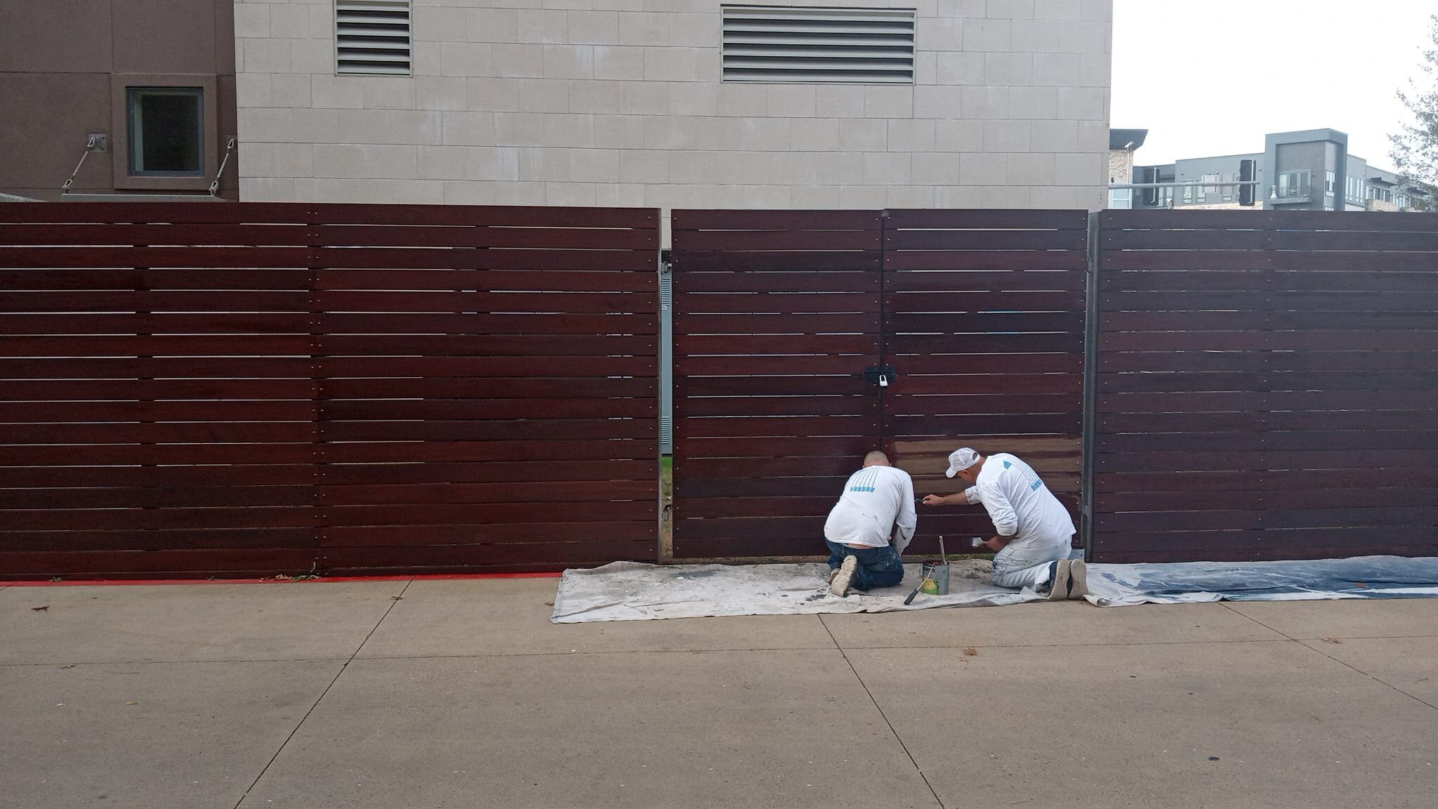 Two workers painting a wooden fence.