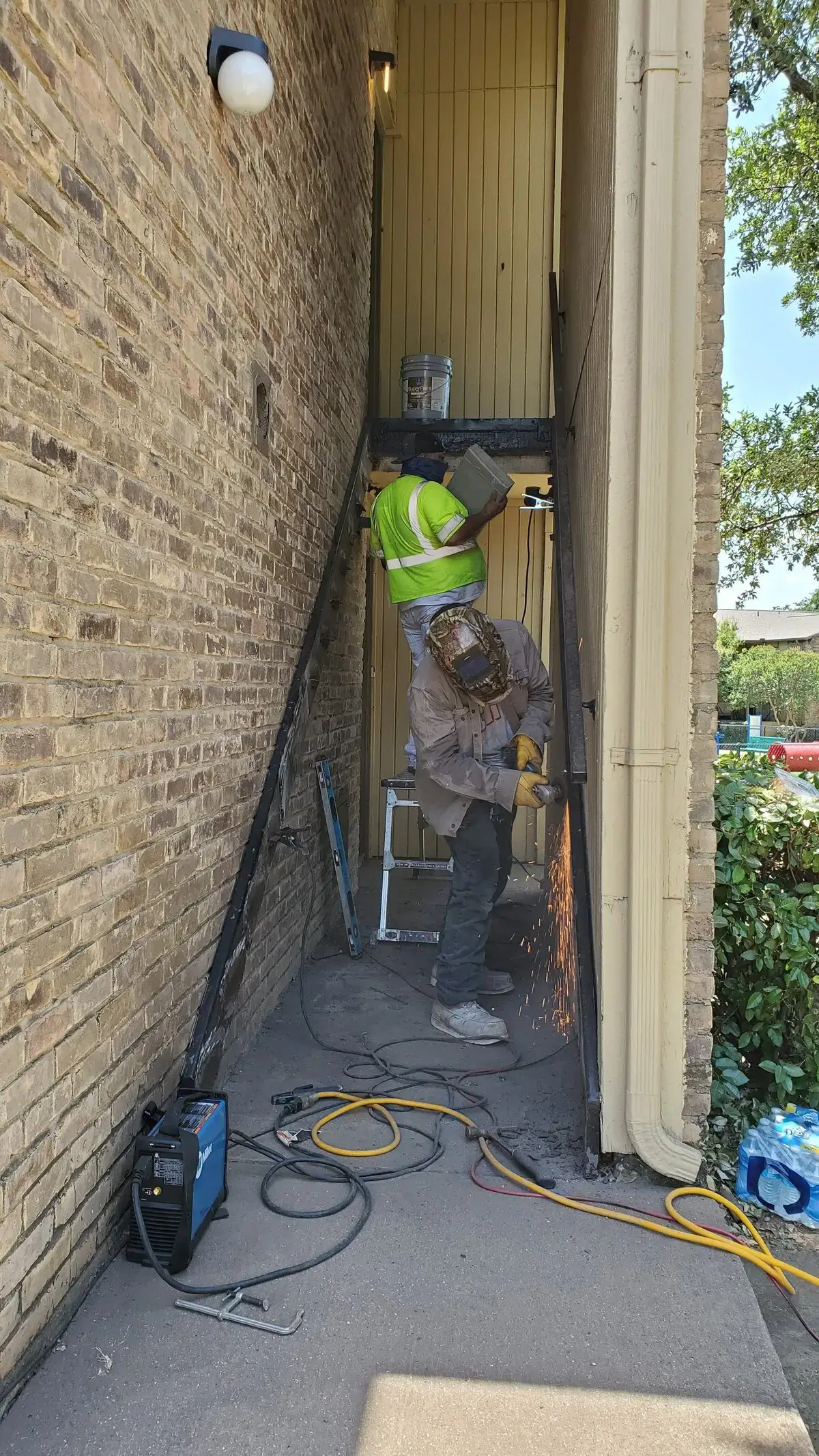 Construction workers welding metal framework outside building.